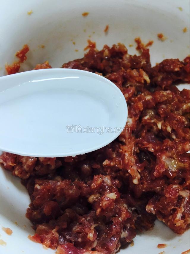 与调料拌匀的肉馅，分三次加入适量清水，顺时针搅拌起胶
