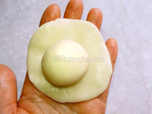 取一片水油皮面团用手掌按扁，按成中间略厚，边缘稍薄的饼皮，中间放上一个油酥面团。