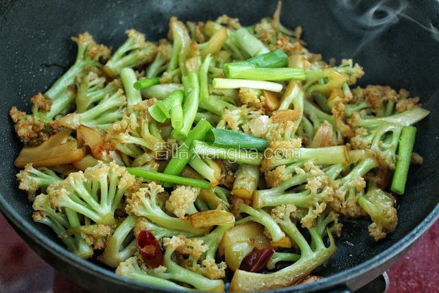 待水分收干、菜花变软时，放入少许盐、糖和葱段翻炒均匀