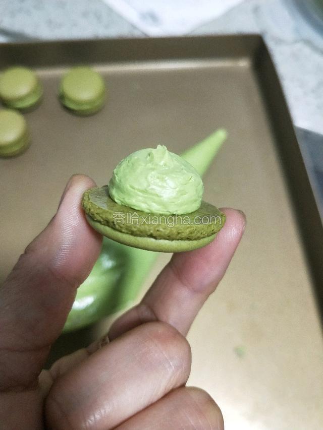 将内馅装入裱花袋。可以用裱花嘴也可以不用装圆形裱花咀，我是没有装的。取一个马卡龙外壳如图挤上抹茶内陷，再盖上一个大小相同的。