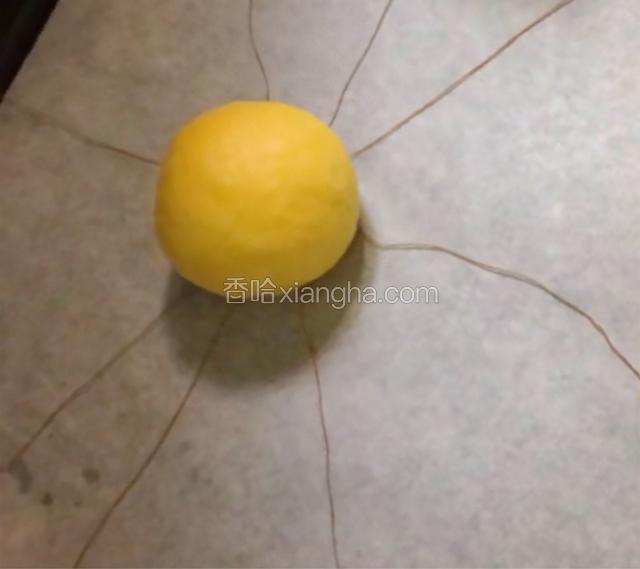 用南瓜面团包住豆沙团并搓圆，收口朝下放棉线中心位置上。