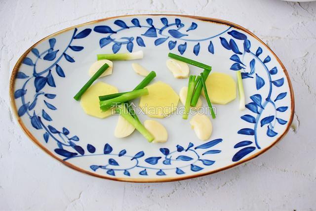 准备一个蒸鱼的盘子，放入一半葱姜蒜垫底