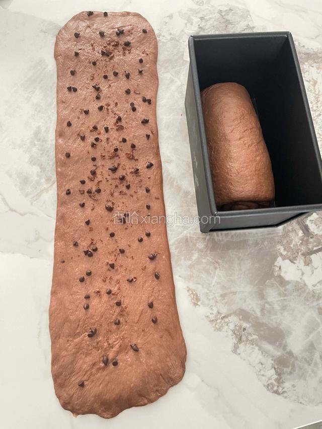 温馨提示，根据我做吐司多年的经验，也是为了节省时间发酵更快，所以我不会去做三卷两擀两松弛，可以参考我的做法：直接将一发好的面团分割成两等份再用擀面杖擀成长条，再放入自己喜欢的耐高温巧克力豆卷起来宽度不要超过吐司盒，如下图。